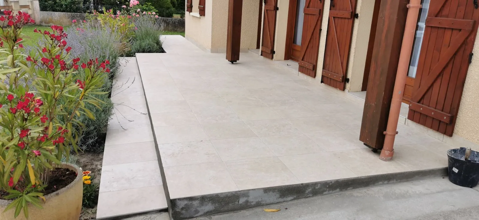 Allée extérieure carrelée le long d'une maison, bordure végétalisée