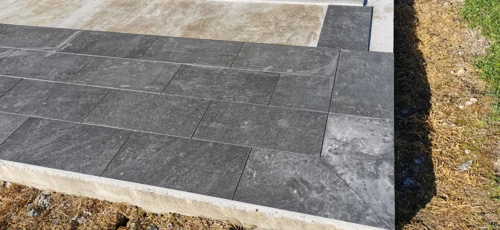 Grande terrasse carrelée en grès cérame gris le long de la façade